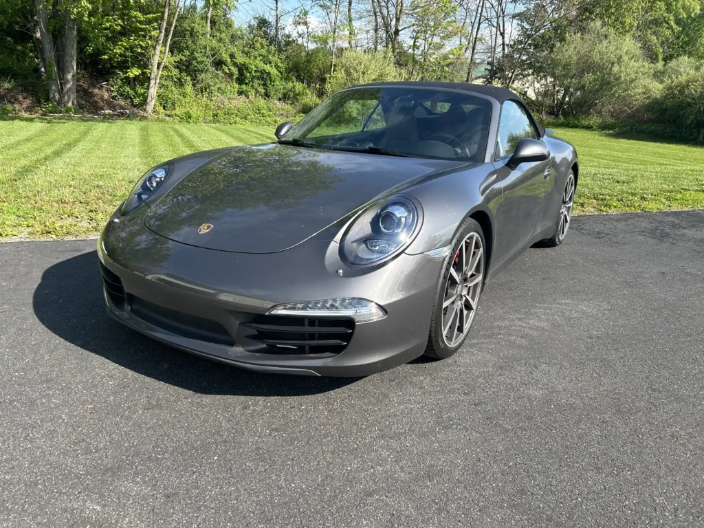 Front three-quarter view of a dark metallic grey Porsche 911 convertible parked outside Skylands Car Audio and Accessories.
